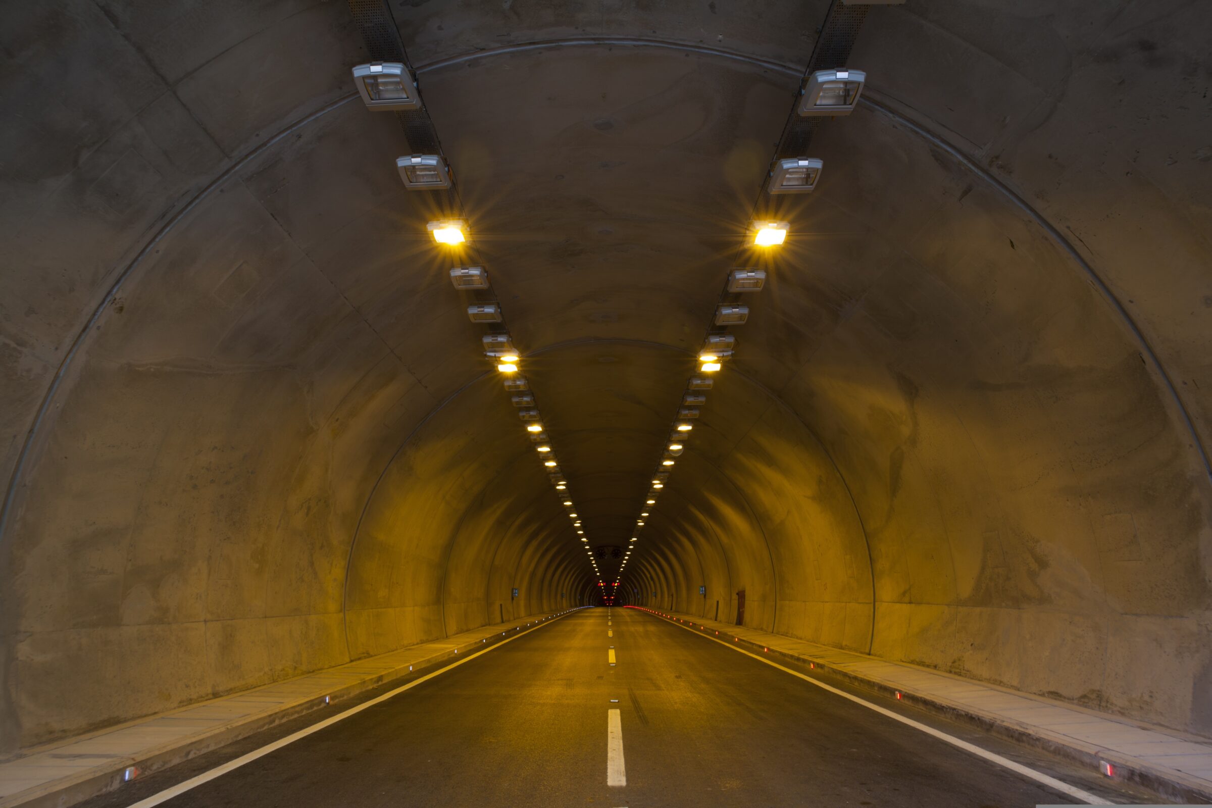 Smooth asphalt road inside a tunnel with bright light ahead—ideal for illustrating durable, high-quality pavement solutions.