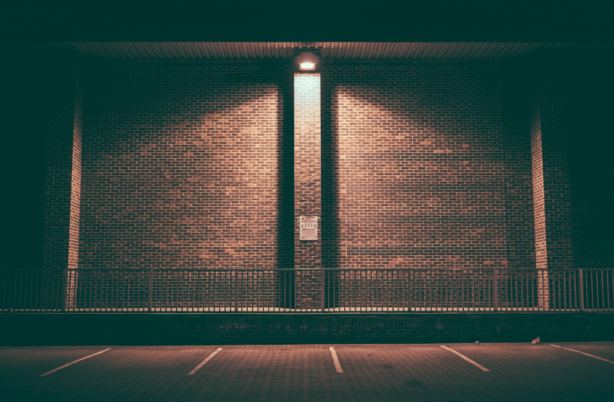 Empty Omaha parking lot at night with white striping, brick wall, and metal railing under a single light.