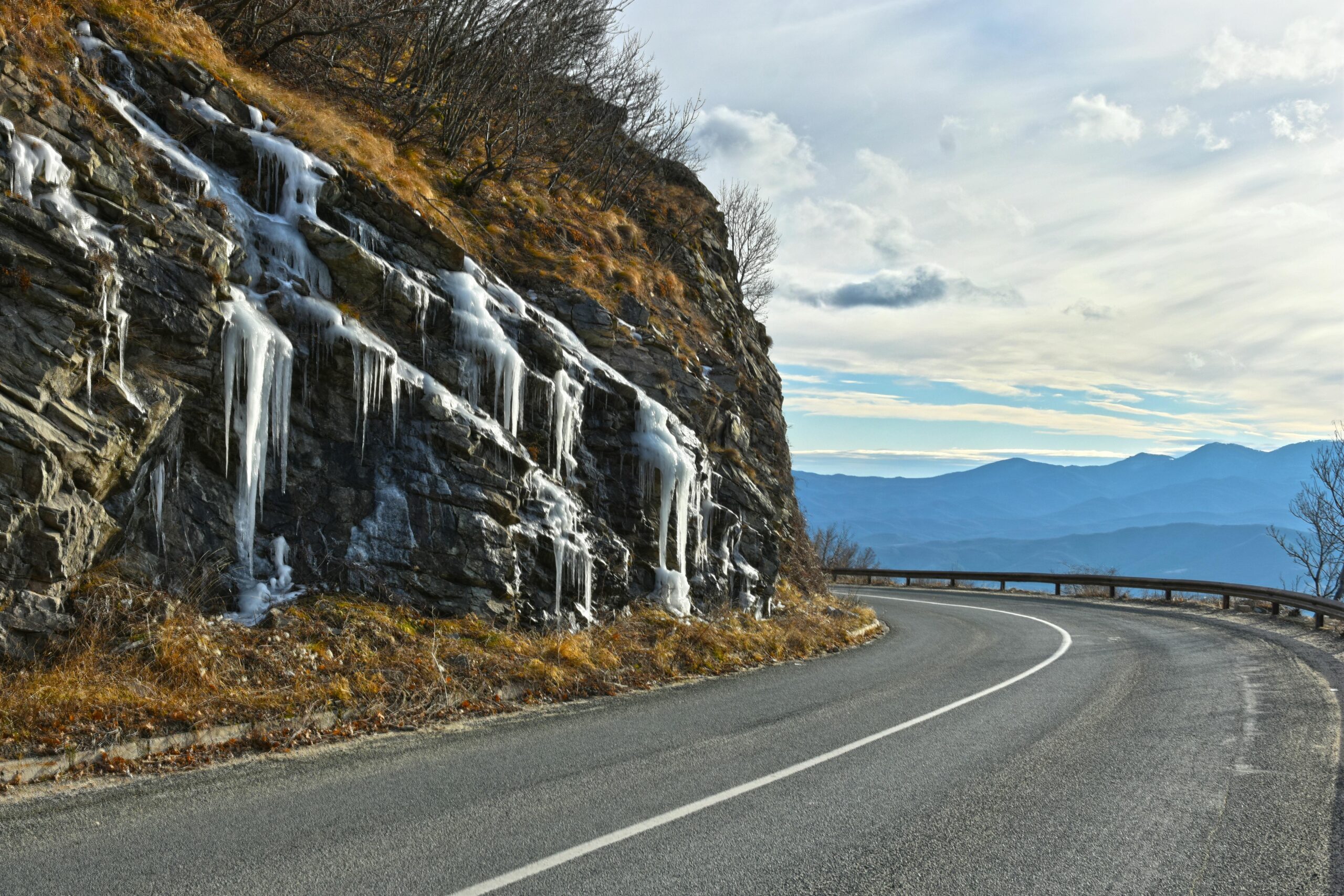 Snow‑covered mountain road with icy curves illustrating how deicing chemicals and freeze‑thaw cycles affect asphalt pavement durability in cold‑weather regions.